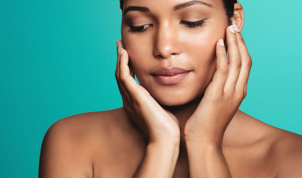 Woman touching her face against a teal background for Lumecca IPL photofacial in London